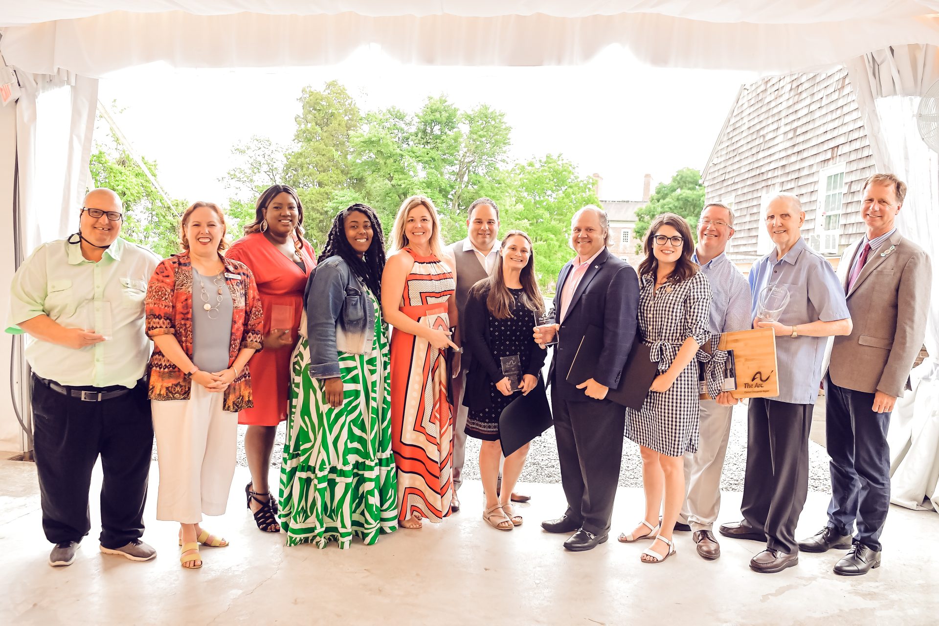 Celebration Impact awardees stand together with their awards. Everyone is smiling, dressed formally. There are trees and natural light in the background.