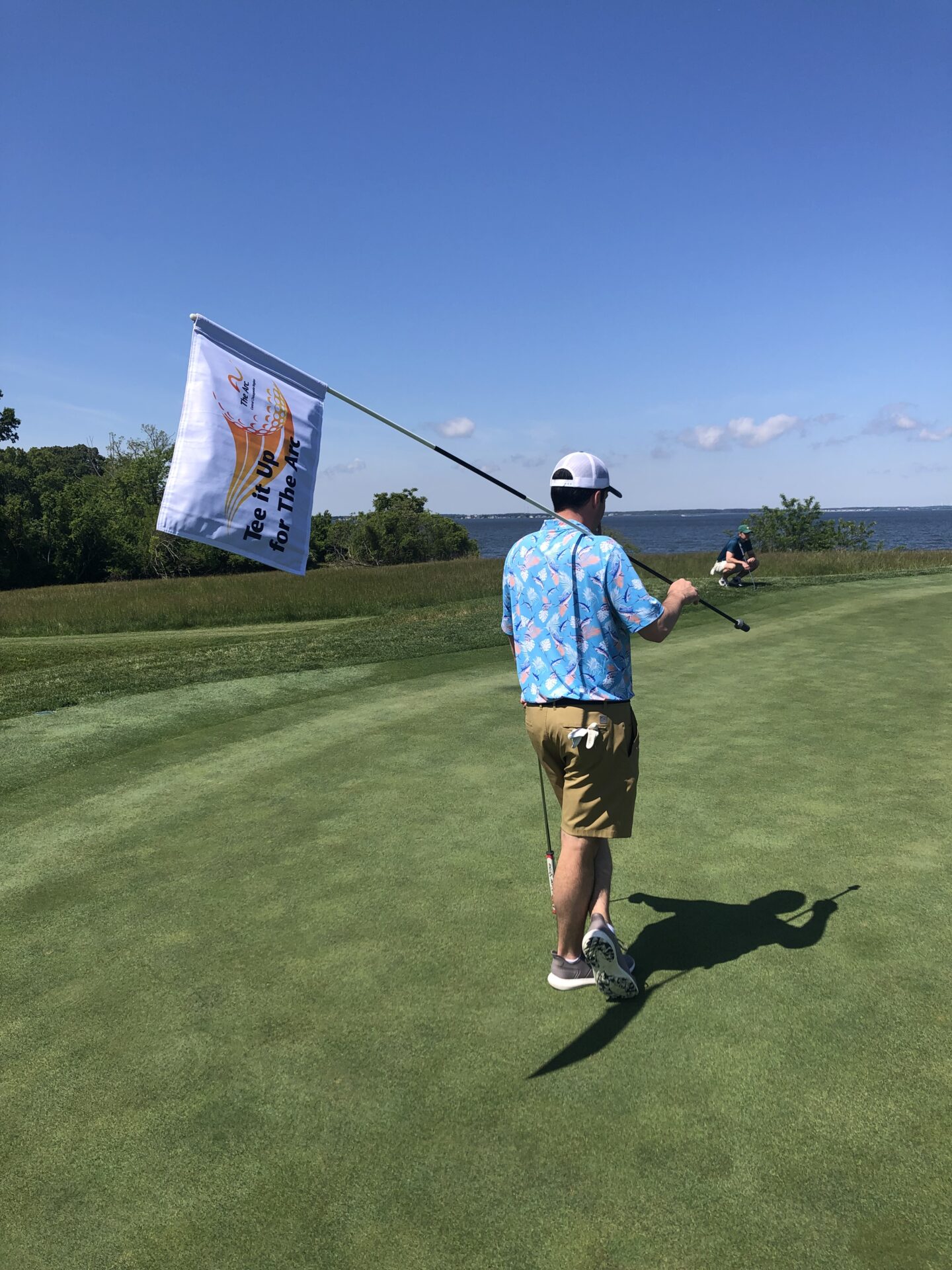 Man holding the flagstick at Tee It Up for The Arc 2024