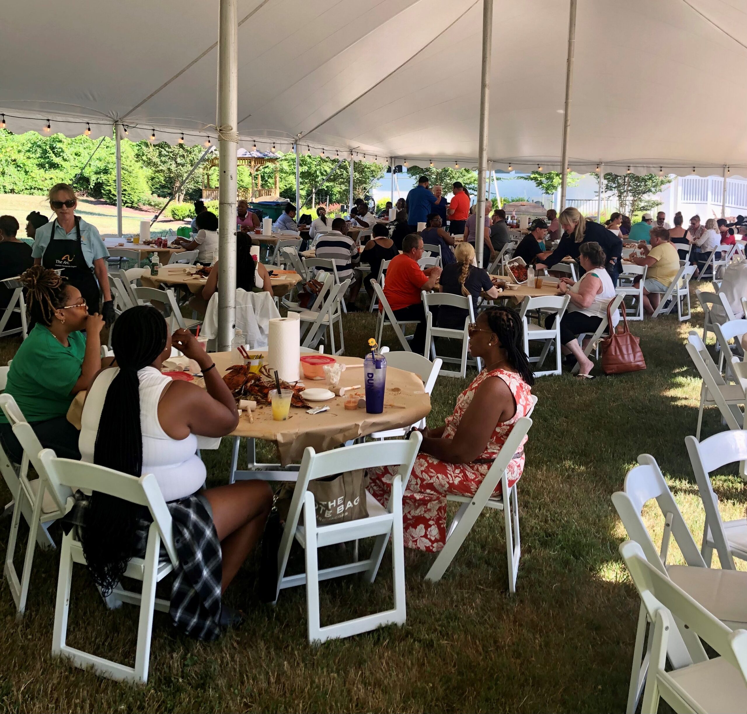 Employees of The Arc sitting at tables under a tent for Celebration Service