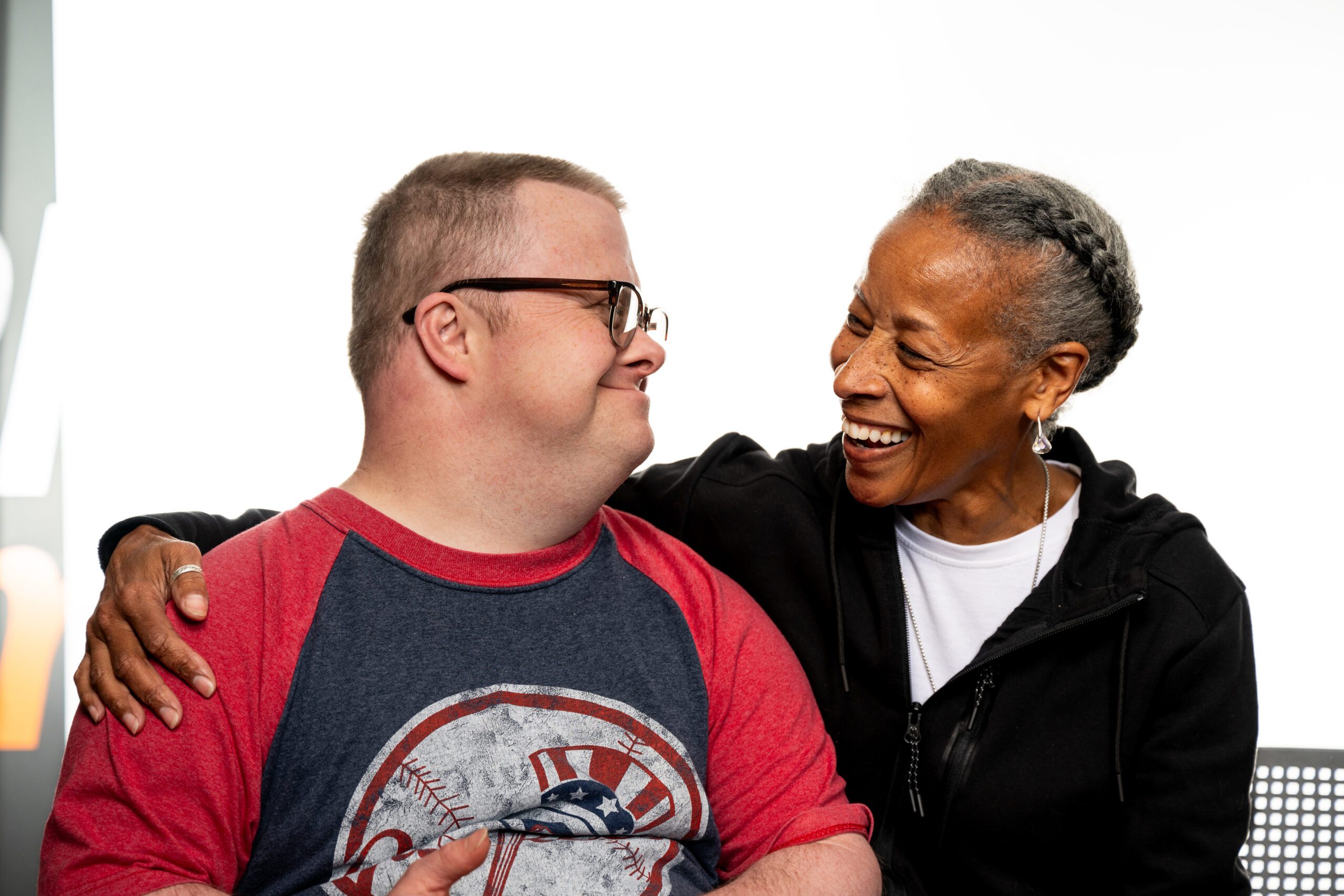 A Health Access Assistant sitting with her arm around the person she supports while they look at each other laughing